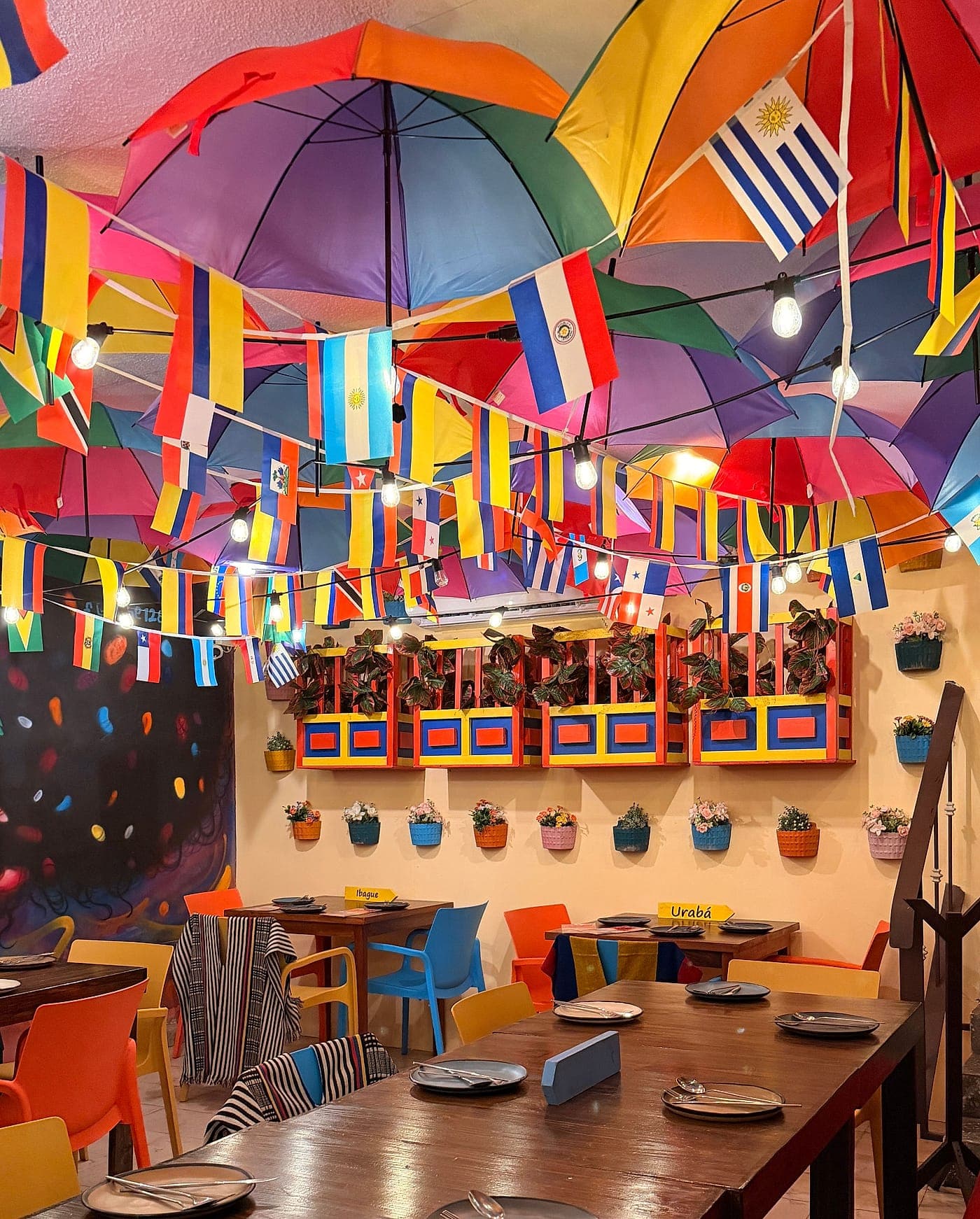 Mesa comunal de madera puesta para diez personas bajo el techo de sombrillas de colores y las banderas de países de Latinoamérica